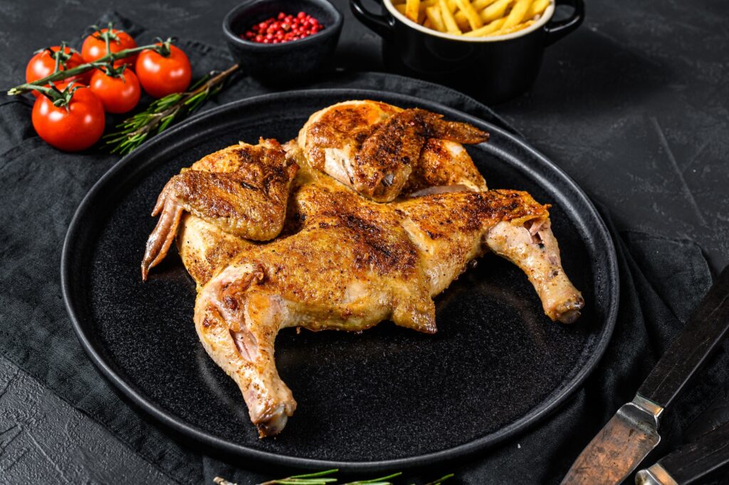 Roasted chicken with rosemary served on black plate. Black background. Top view